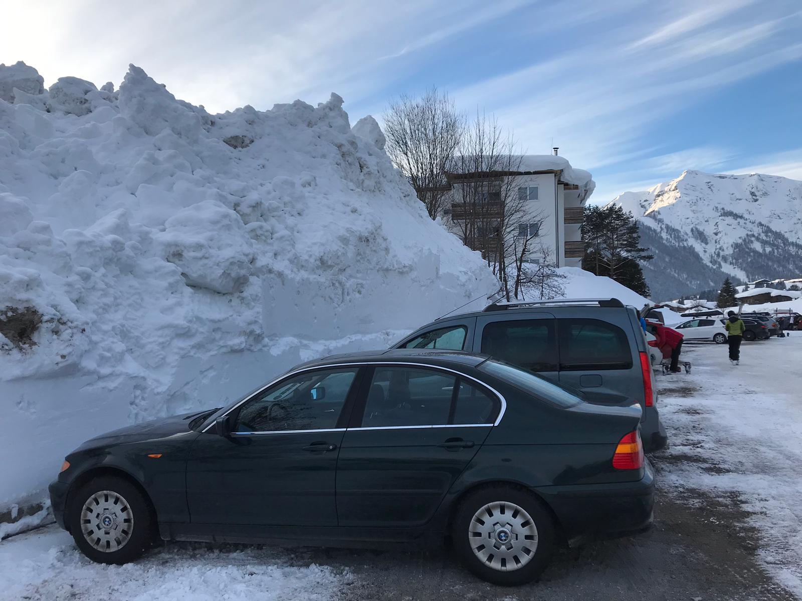 Blaues Auto auf Parkplatz inmitten rießiger Schneeberge. Ort in Österreich.